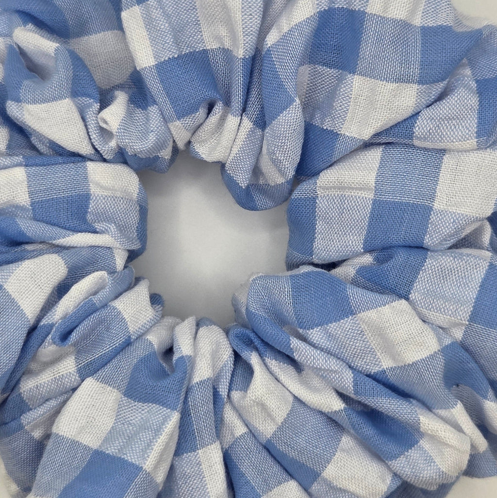 A fabric hair scrunchie with a blue and white gingham checkered pattern, photographed on a plain off-white background.