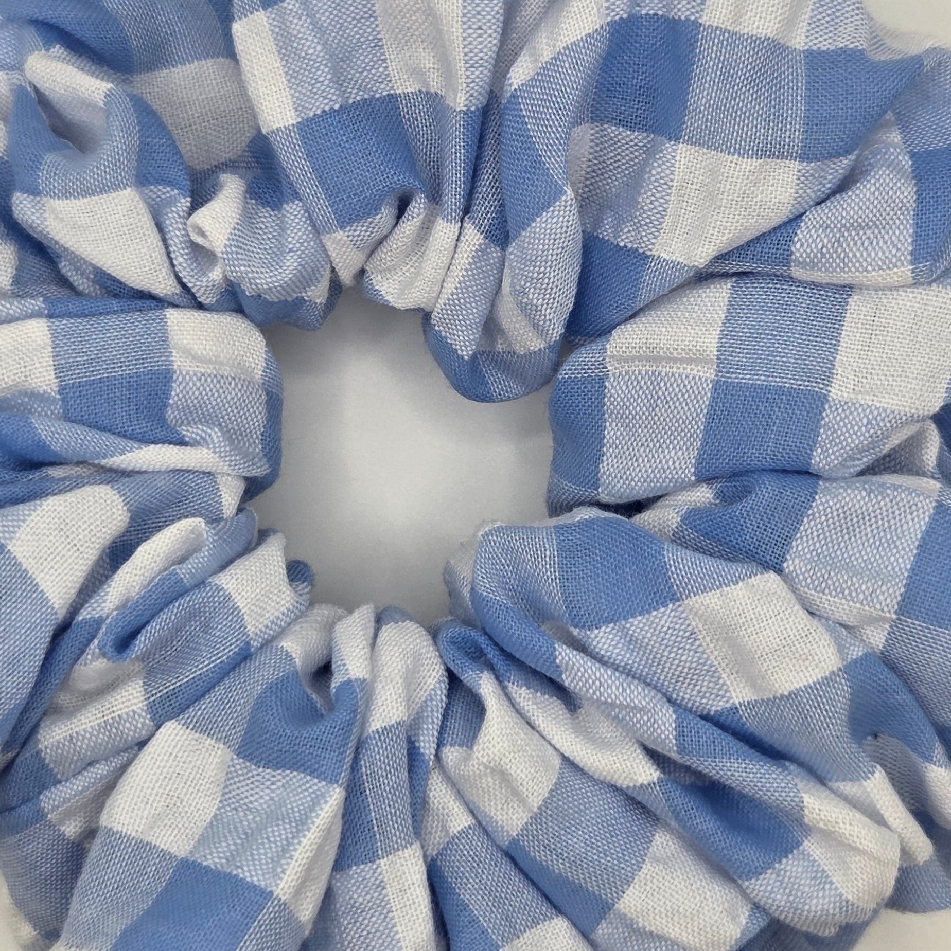 A fabric hair scrunchie with a blue and white gingham checkered pattern, photographed on a plain off-white background.