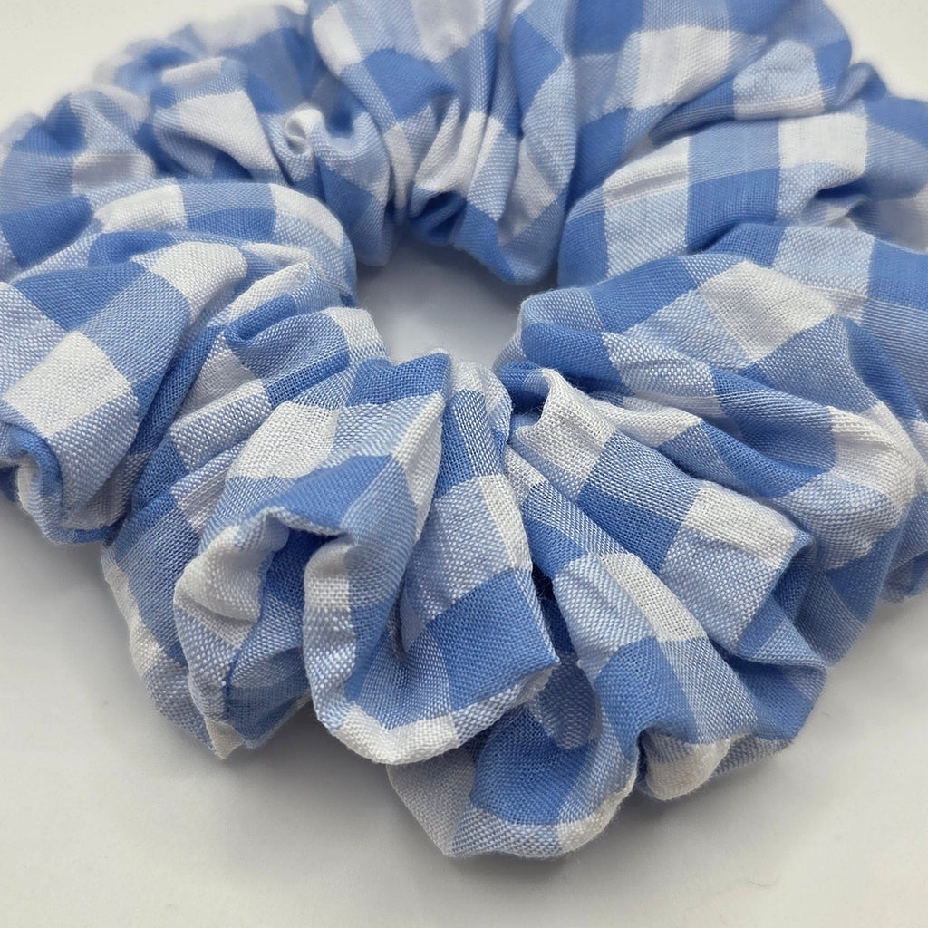 A fabric scrunchie with a light blue and white gingham checkered pattern, photographed on a plain off-white background.