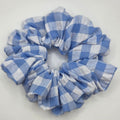 A blue and white gingham checkered fabric scrunchie, photographed from above on a plain white surface.