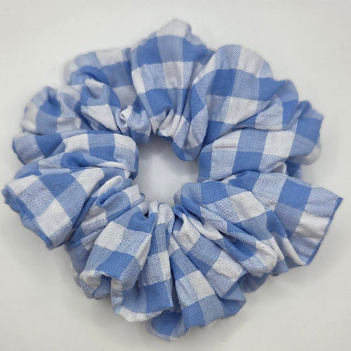 A blue and white gingham checkered fabric scrunchie, photographed from above on a plain white surface.