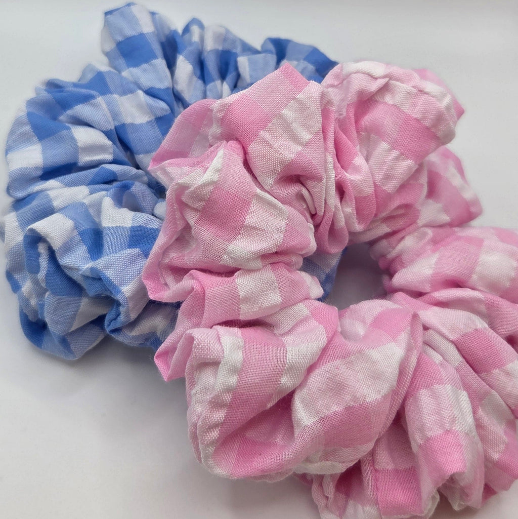 Two fabric hair scrunchies stacked on a plain light background, one in pink and white gingham check and one in blue and white gingham check.