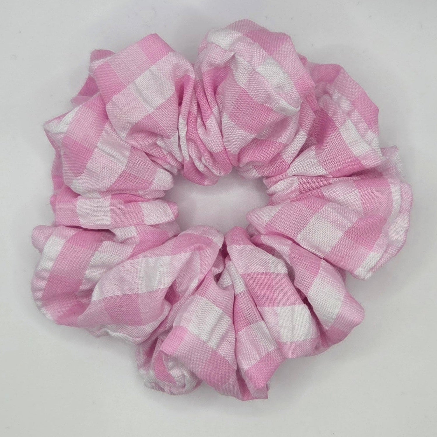 A fabric hair scrunchie with a pink and white gingham checkered pattern, photographed on a plain white background.