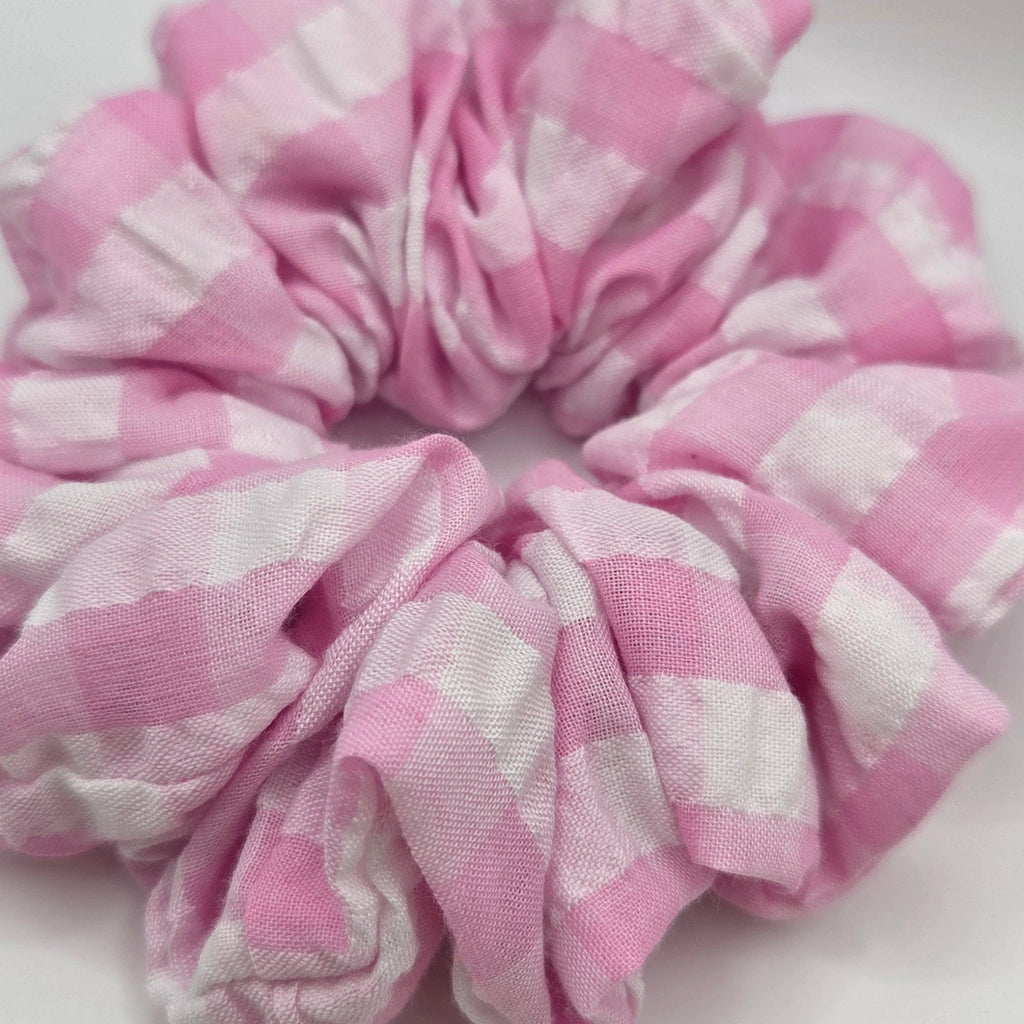 A pink and white checkered fabric scrunchie on a plain light background.