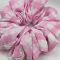 A pink and white checkered fabric scrunchie on a plain light background.