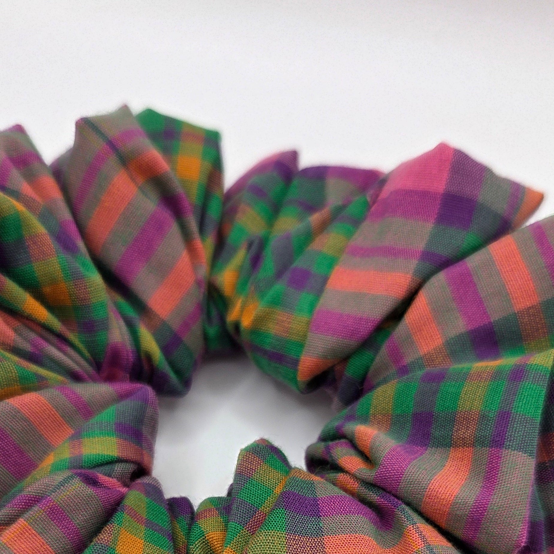 A fabric scrunchie with a plaid pattern in purple, green, orange, and pink, shown on a plain white background.