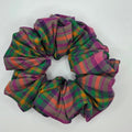 A fabric hair scrunchie with a multicolor plaid pattern in purple, green, orange, and pink, resting on a plain white surface.
