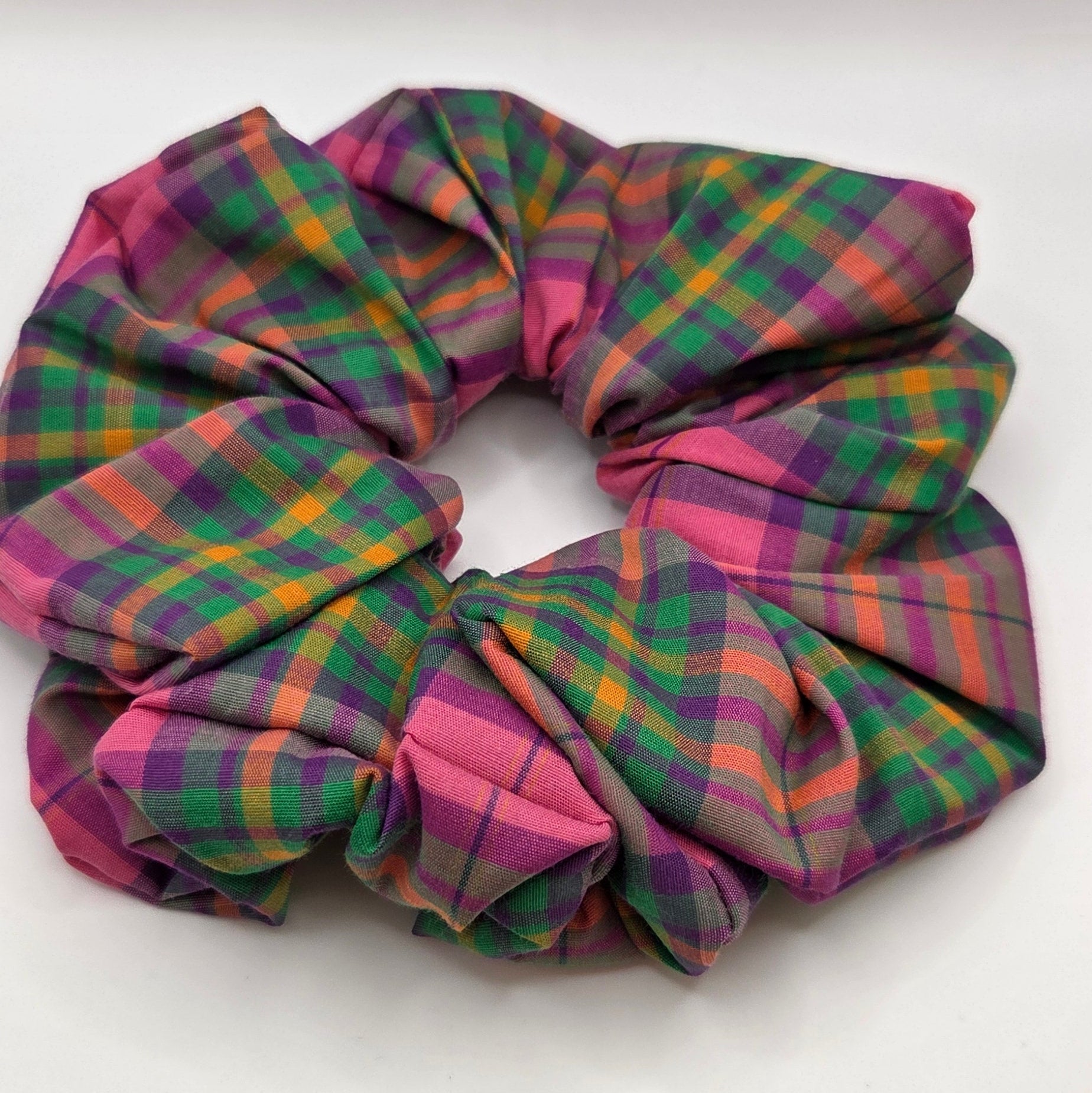 A fabric scrunchie with a pink, green, and orange plaid pattern, photographed on a plain white surface.