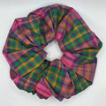 A fabric hair scrunchie with a multicolor plaid pattern in green, pink, and orange, shown on a plain white surface.