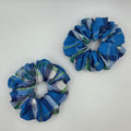 Two fabric scrunchies with a blue, green, and white plaid pattern, displayed on a plain white surface.