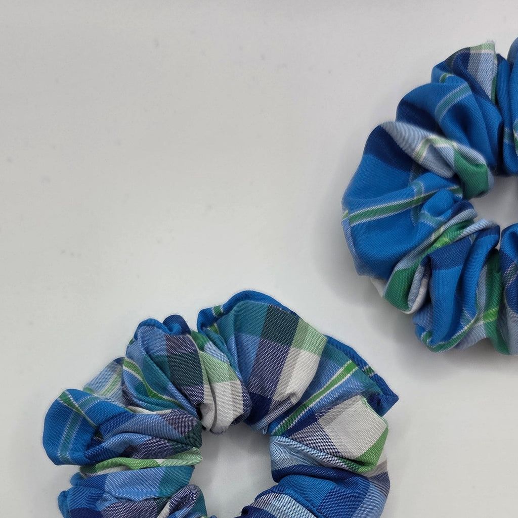 Two fabric hair scrunchies with a blue, green, and white plaid pattern, shown on a plain white background.