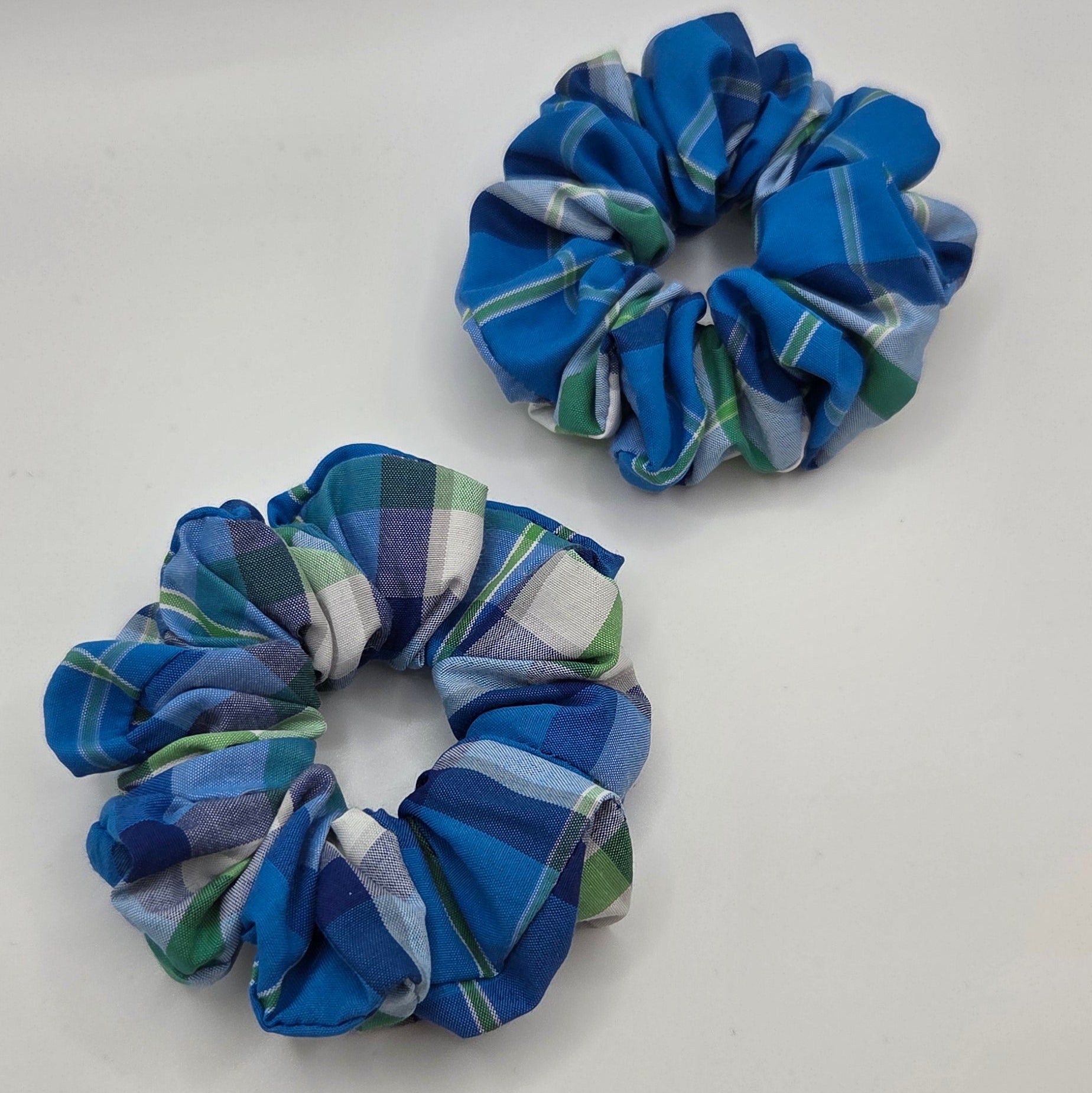 Two fabric hair scrunchies with a blue, green, and white plaid pattern, displayed on a plain white surface.