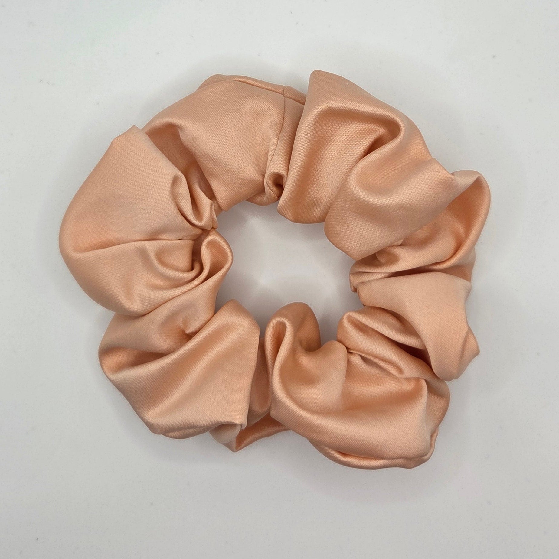 A light peach satin scrunchie with a soft sheen, photographed from above on a plain white background.