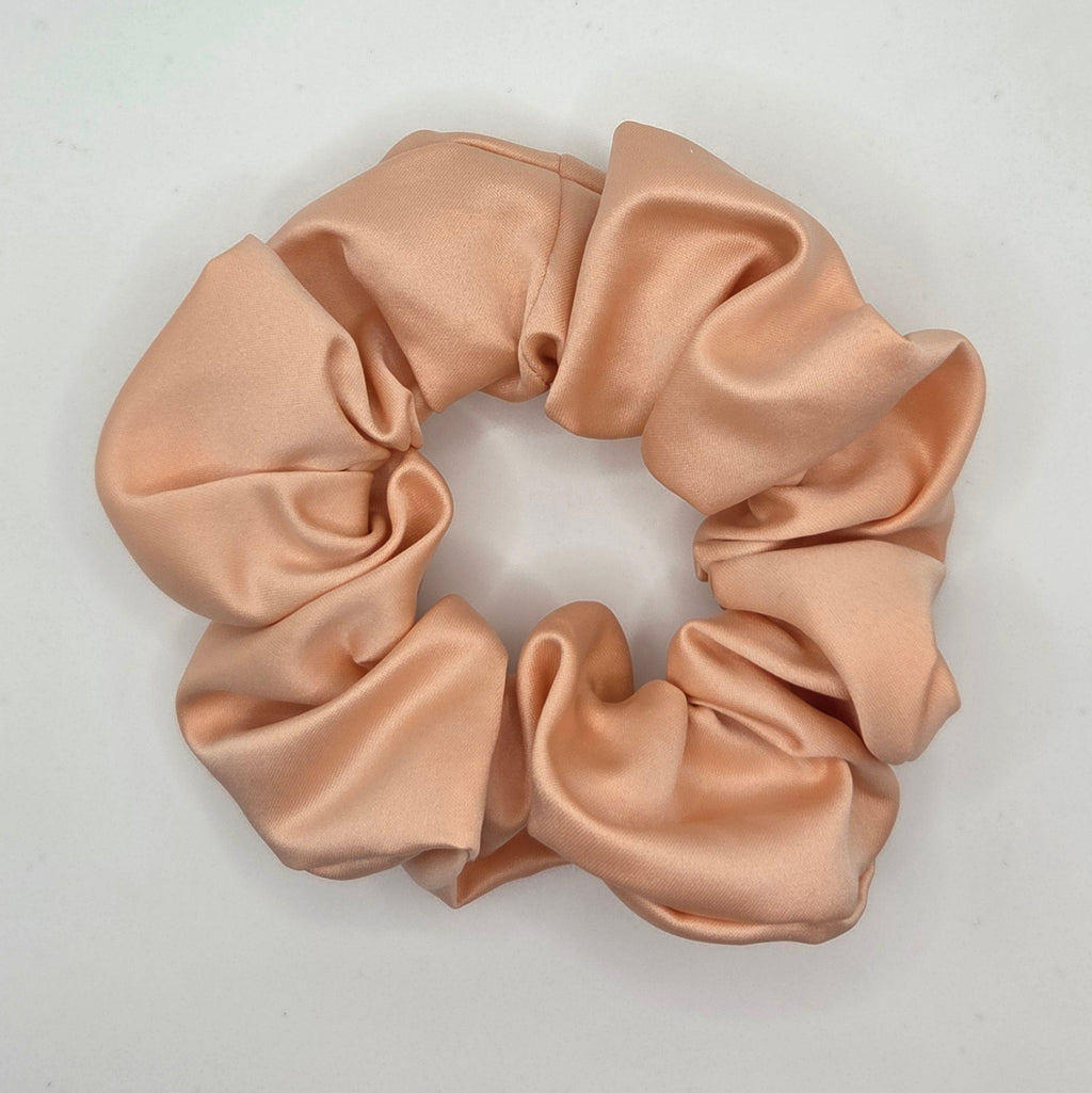A single satin hair scrunchie in a light peach-beige color, photographed from above on a plain white background.