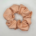 A single satin hair scrunchie in a light peach-beige color, photographed from above on a plain white background.