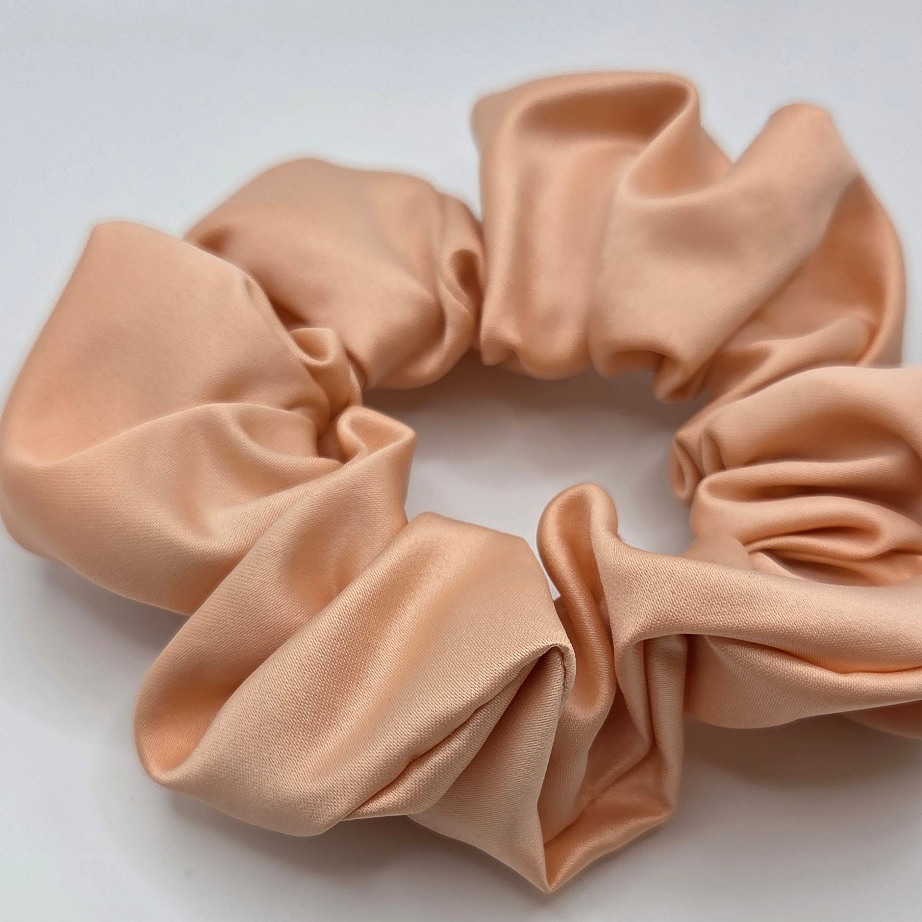 A single fabric hair scrunchie in a soft nude beige color, photographed against a plain light gray background.
