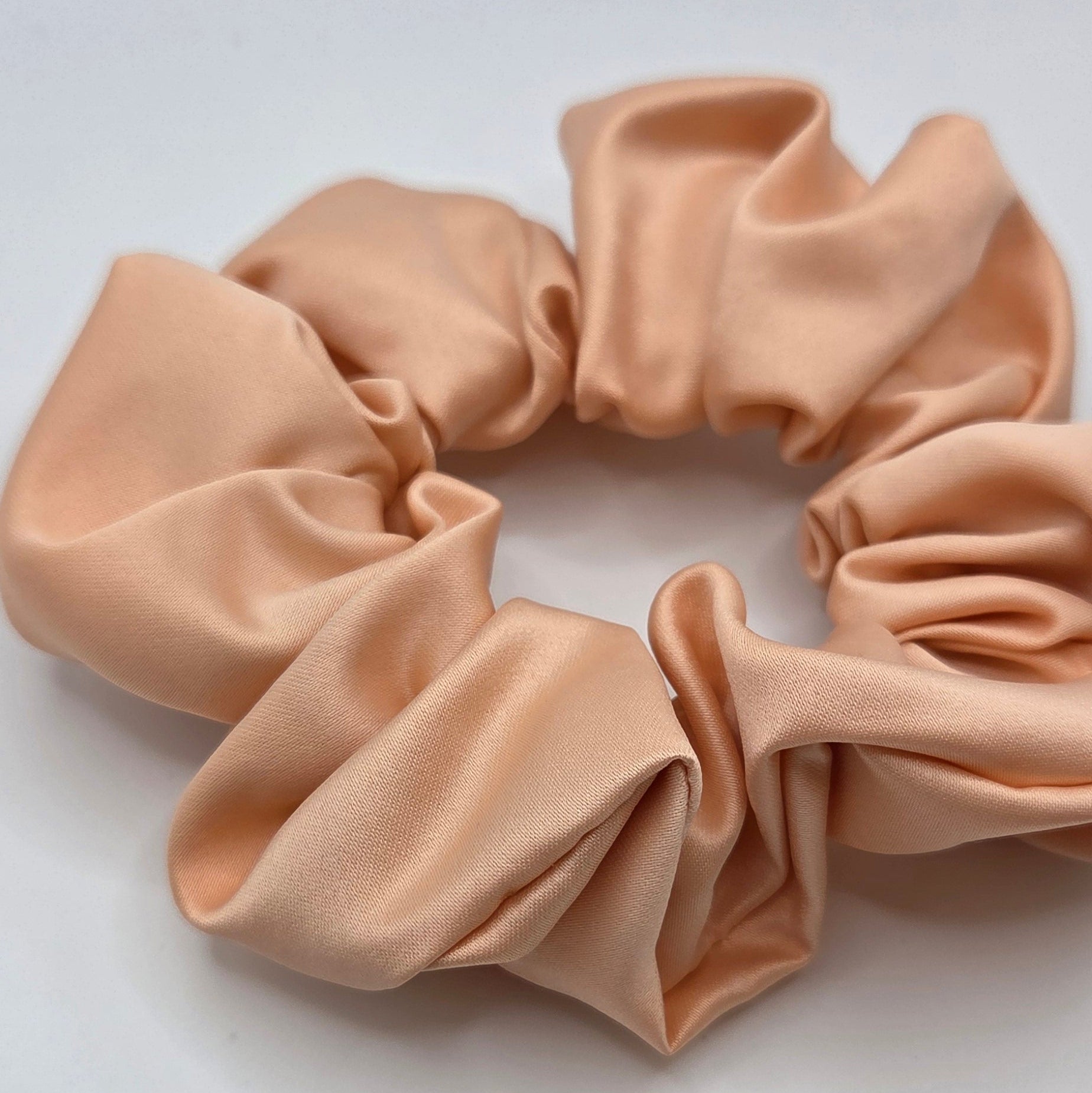 A single satin scrunchie in a light peach-beige color, photographed on a plain white background.