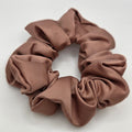 A single fabric scrunchie in a muted taupe-brown color, photographed from above on a plain light background.