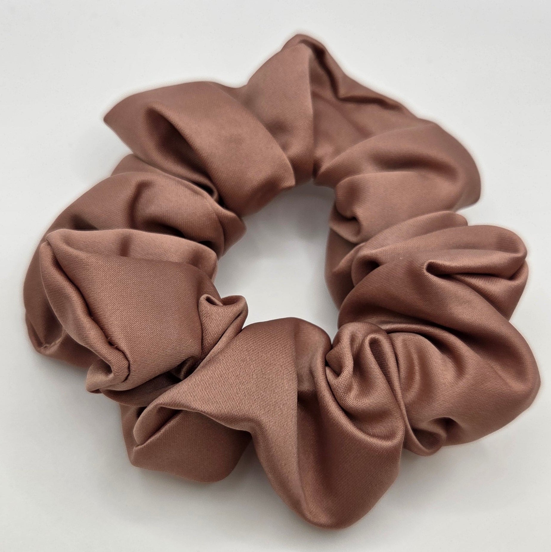 A single fabric scrunchie in a muted taupe-brown color, photographed from above on a plain light background.