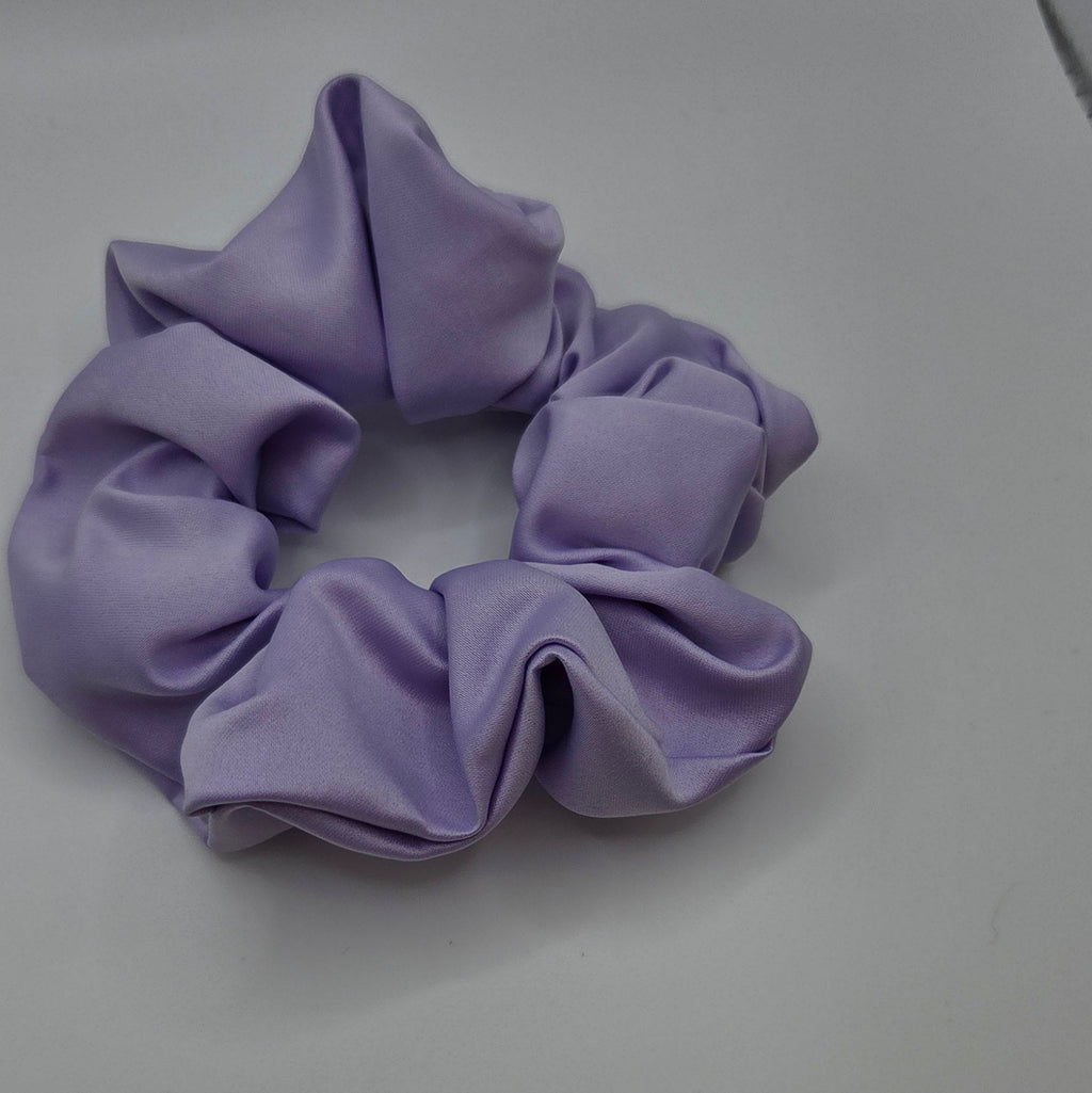 A lavender purple fabric scrunchie on a plain light gray surface.