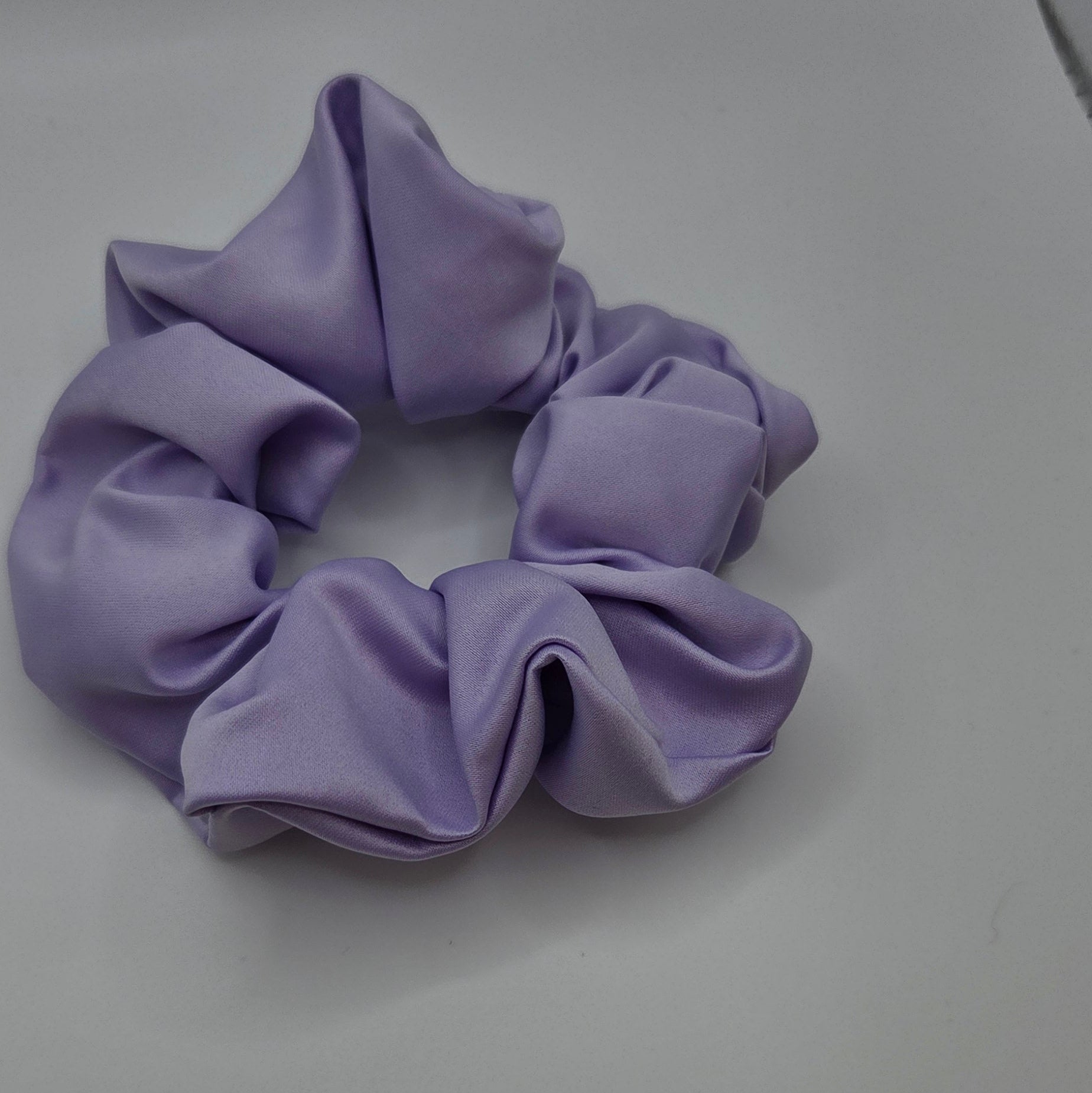 A lavender purple fabric scrunchie on a plain light gray surface.