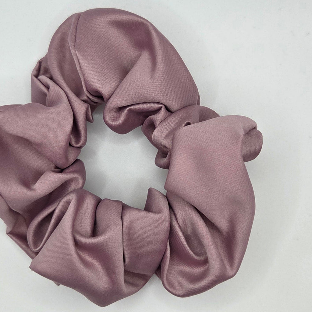 A dusty rose satin hair scrunchie displayed on a plain white surface.
