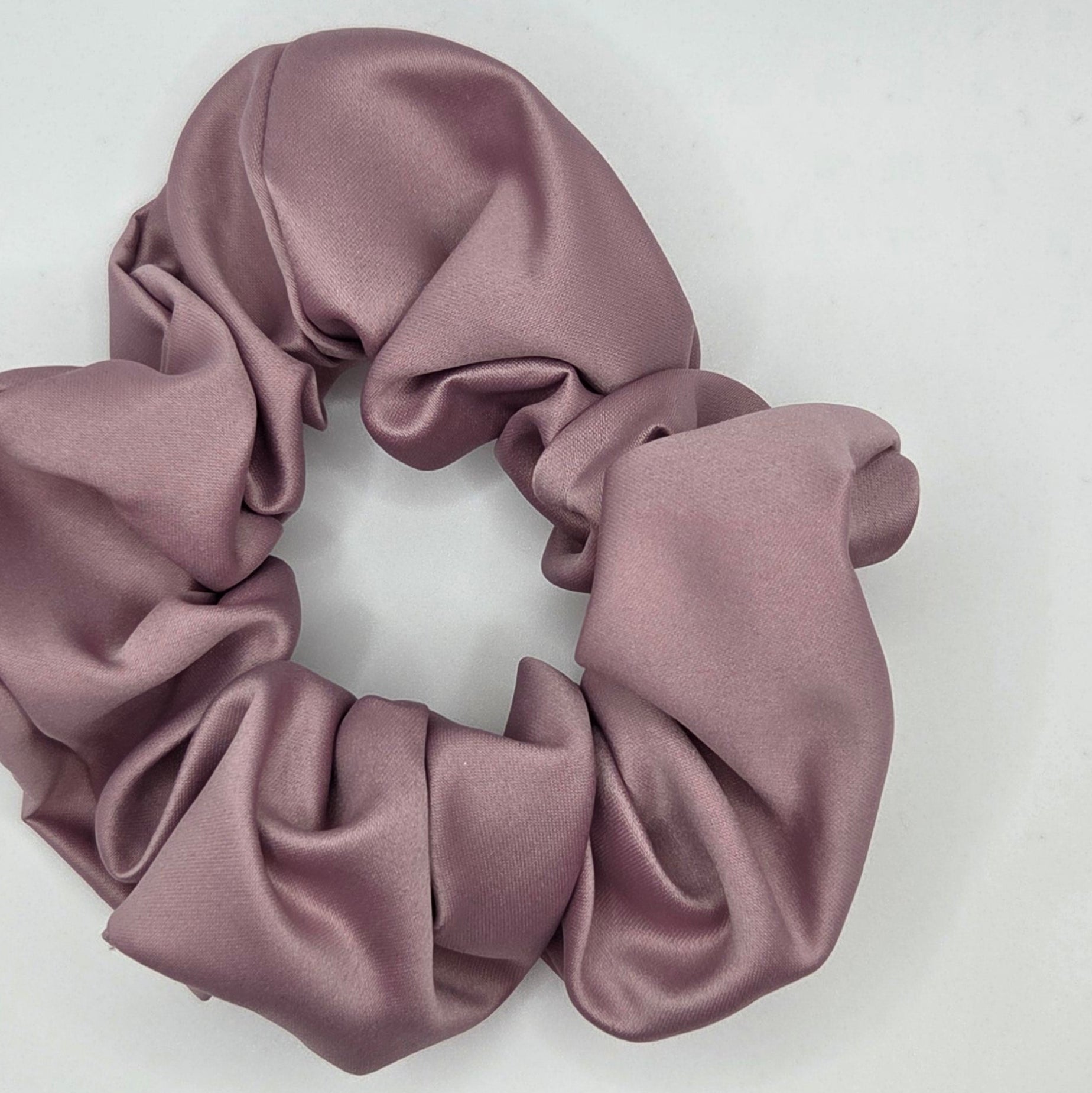 A dusty rose satin hair scrunchie displayed on a plain white surface.