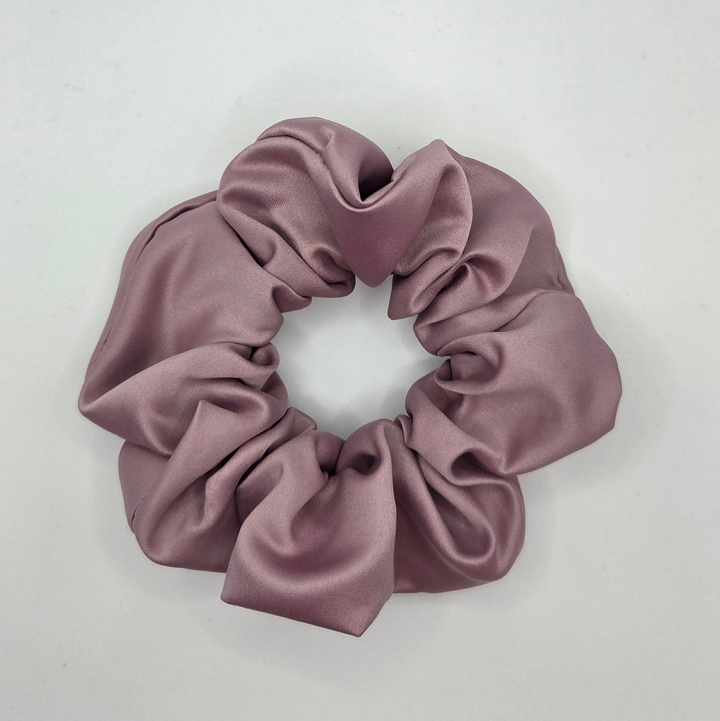 A dusty mauve satin hair scrunchie resting on a plain white surface.