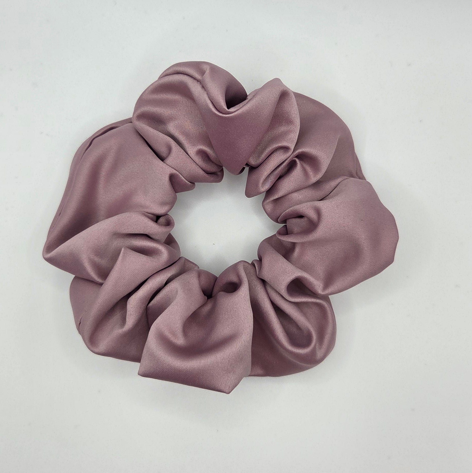 A dusty mauve satin hair scrunchie displayed on a plain white surface.