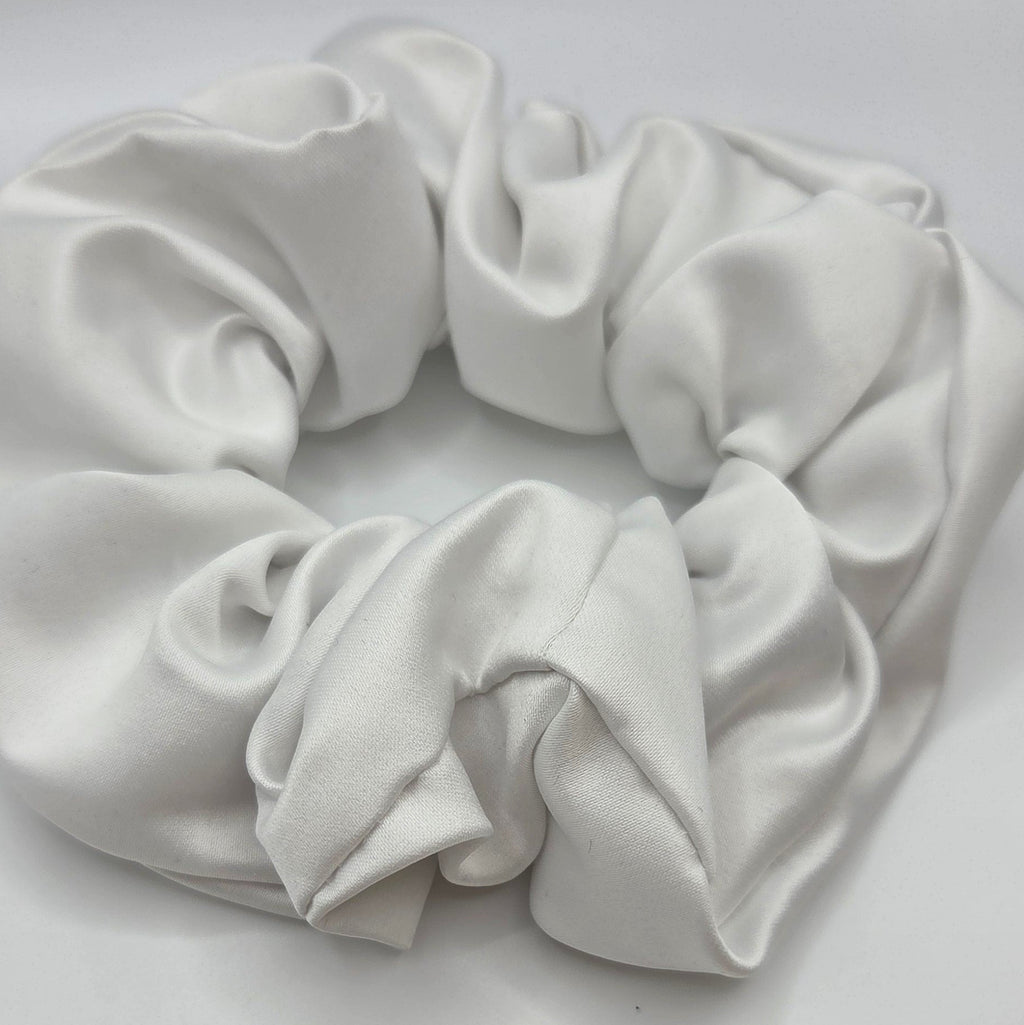 A white satin or silk scrunchie with a soft, draped texture, photographed on a plain light gray background.