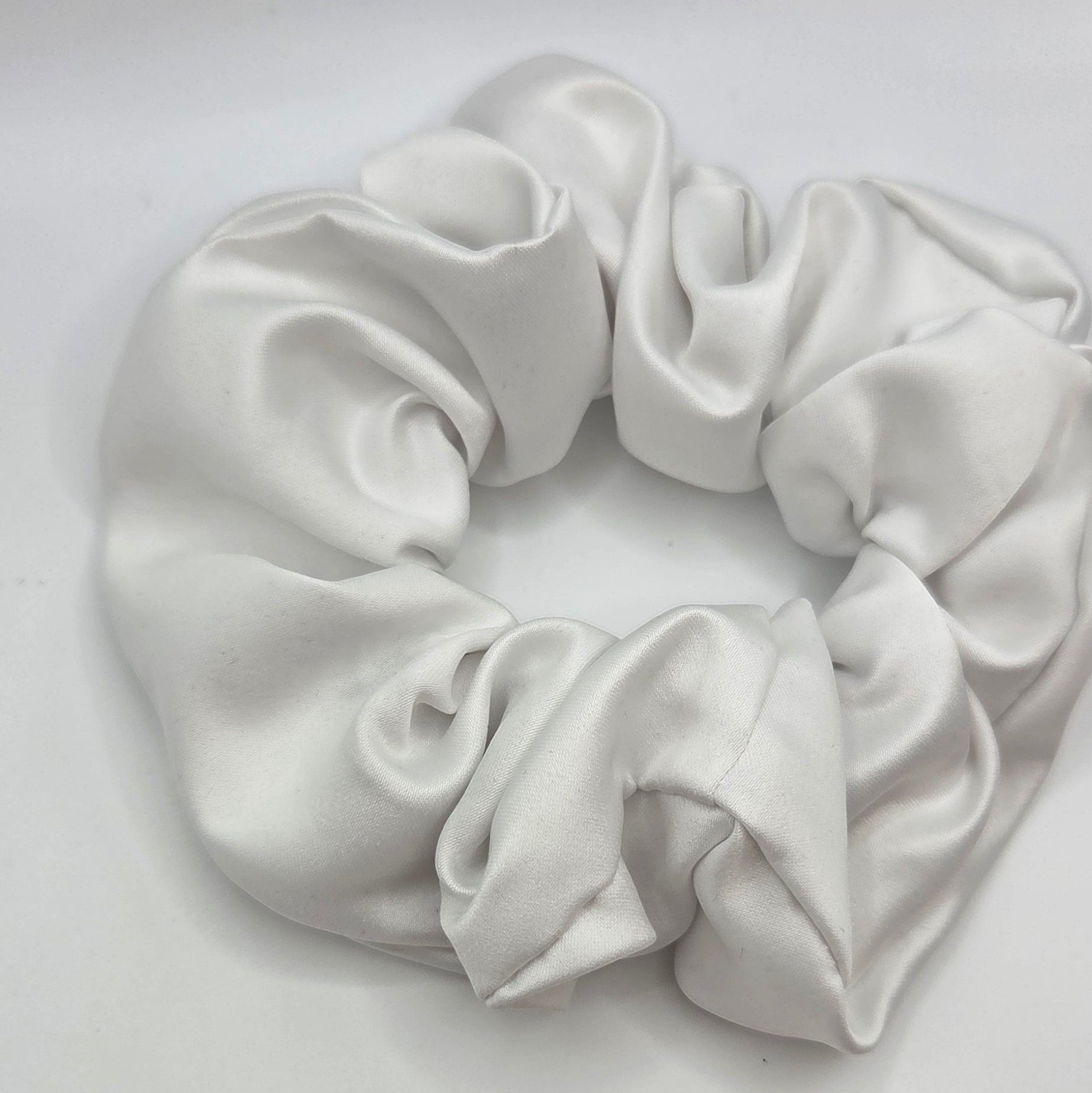 A white satin hair scrunchie with a soft, lustrous sheen, photographed on a plain light gray background.