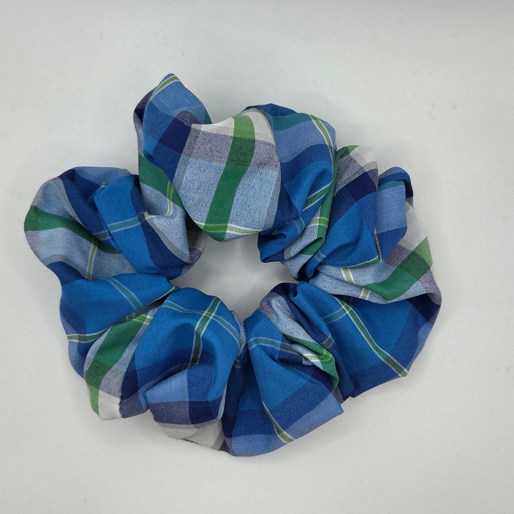 A fabric hair scrunchie with a blue, green, and white plaid pattern, photographed on a plain white surface.