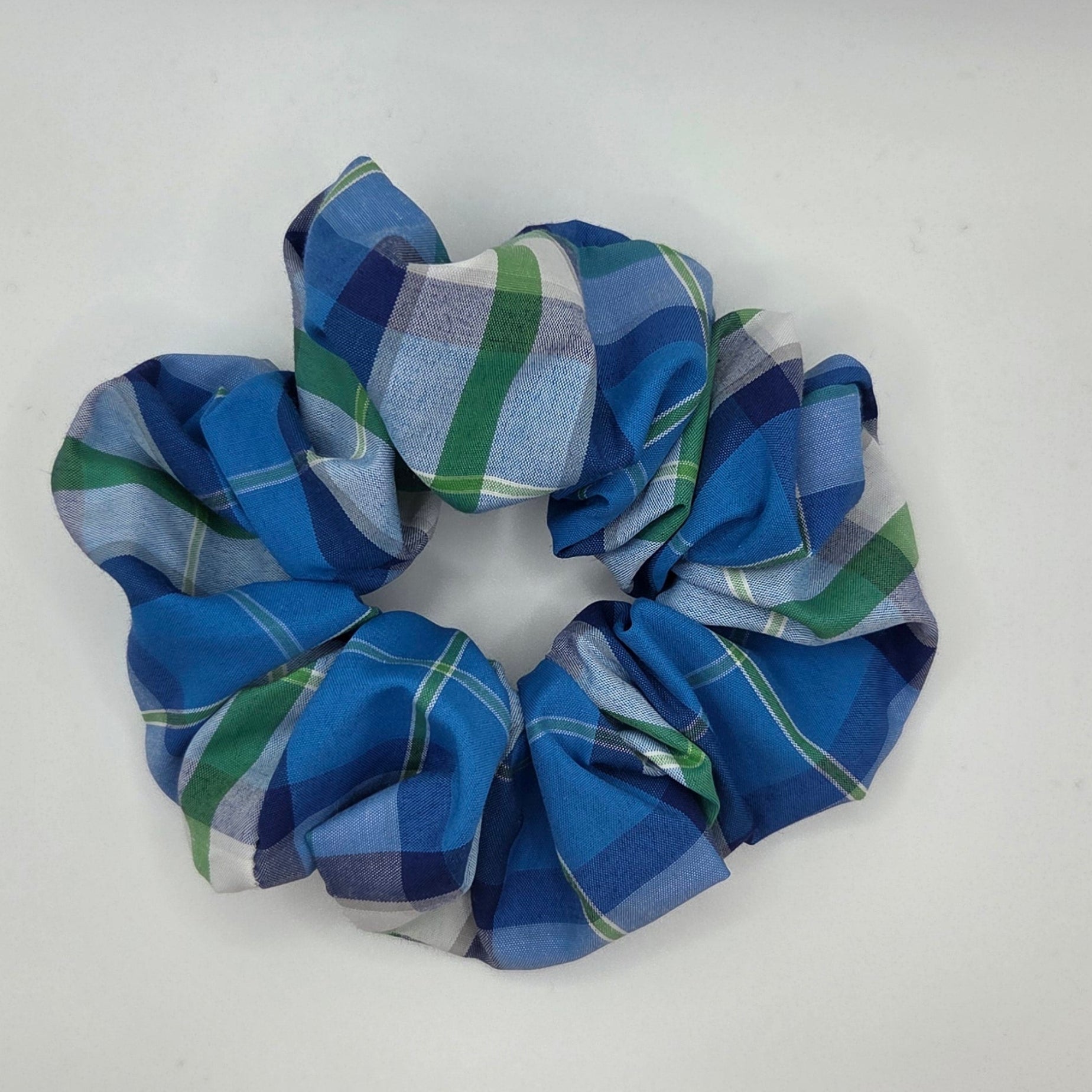 A fabric hair scrunchie with a blue, green, and white plaid pattern, photographed on a plain white surface.