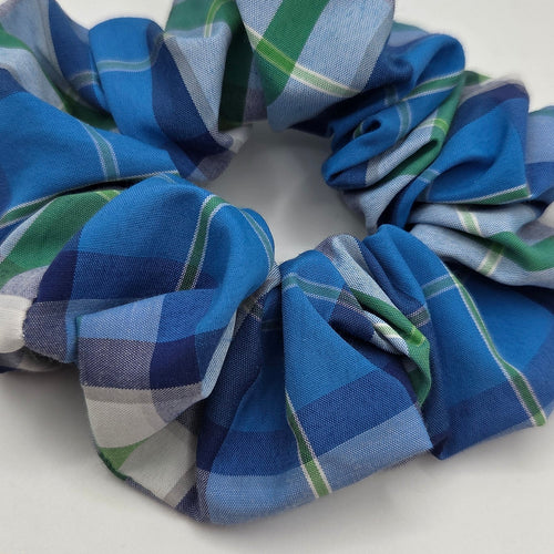 A fabric hair scrunchie with a blue, green, and white plaid pattern, photographed on a plain light gray background.