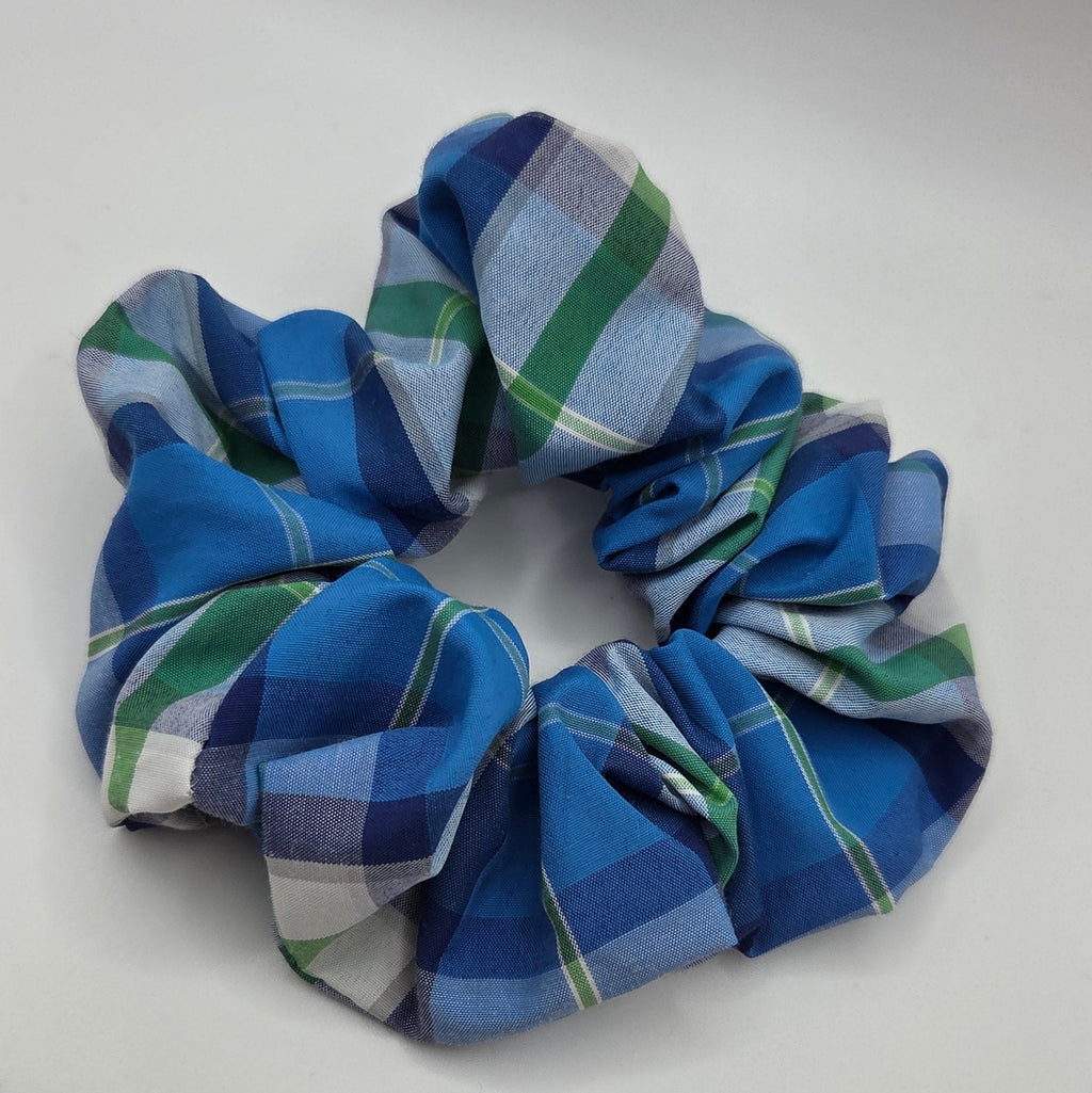 A fabric scrunchie with a blue, green, and white plaid pattern, photographed on a plain light gray background.