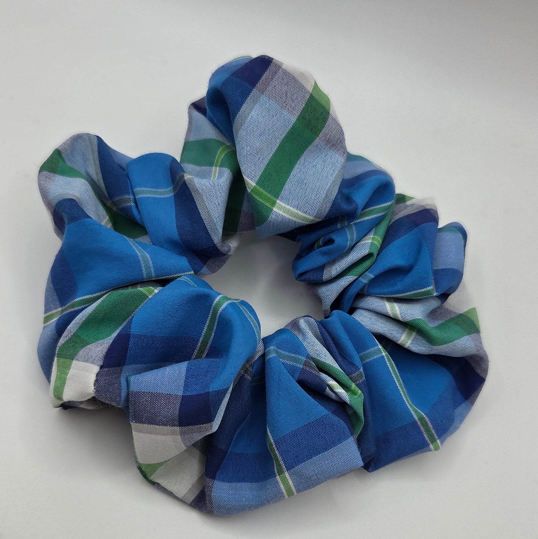 A fabric scrunchie with a blue, green, and white plaid pattern, photographed on a plain light gray background.
