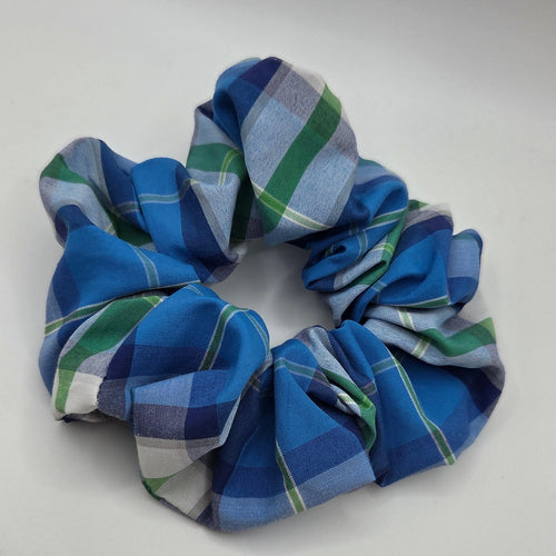 A fabric scrunchie with a blue, green, and white plaid pattern, photographed on a plain light gray background.