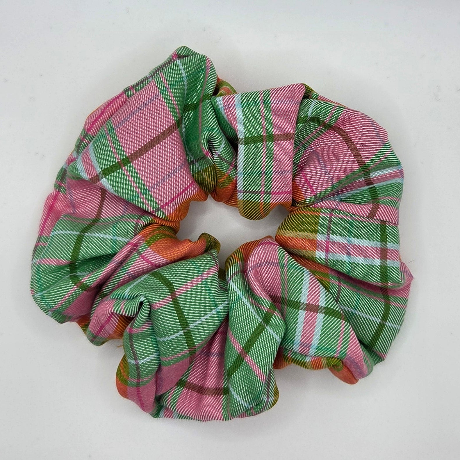 A fabric hair scrunchie with a pink, green, and white plaid pattern, photographed on a plain white background.