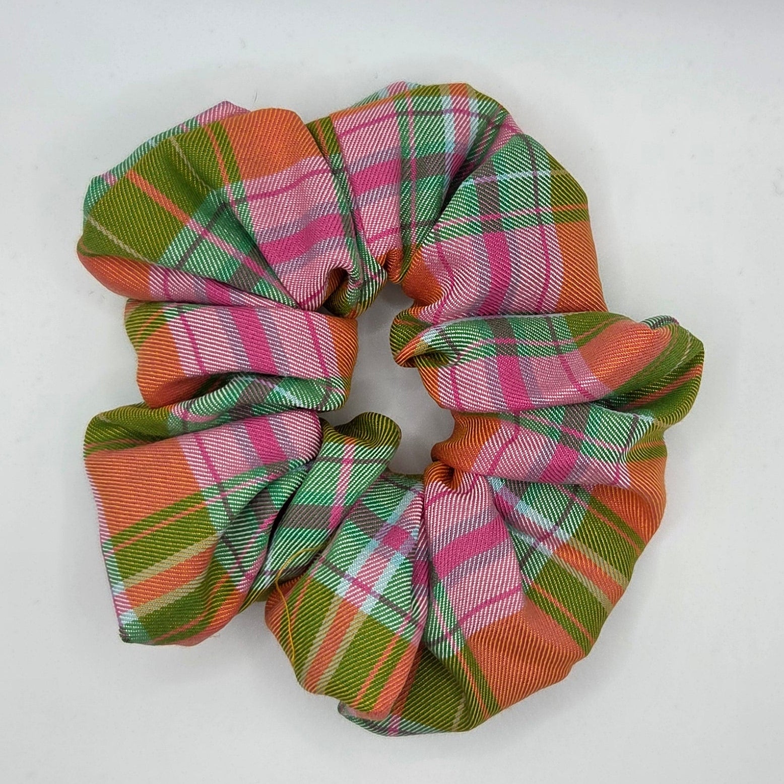 A fabric hair scrunchie with a plaid pattern in pink, green, and orange, shown on a plain white background.