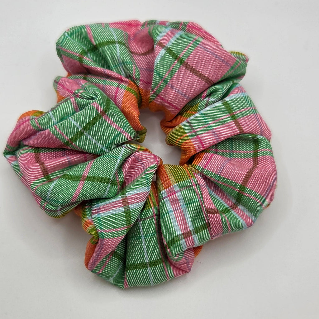 A fabric scrunchie with a pink, green, and white plaid pattern, photographed on a plain light gray background.